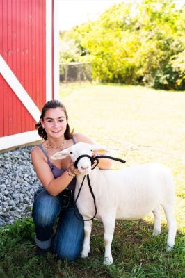 Cassidy with a sheep in front of a red barn door