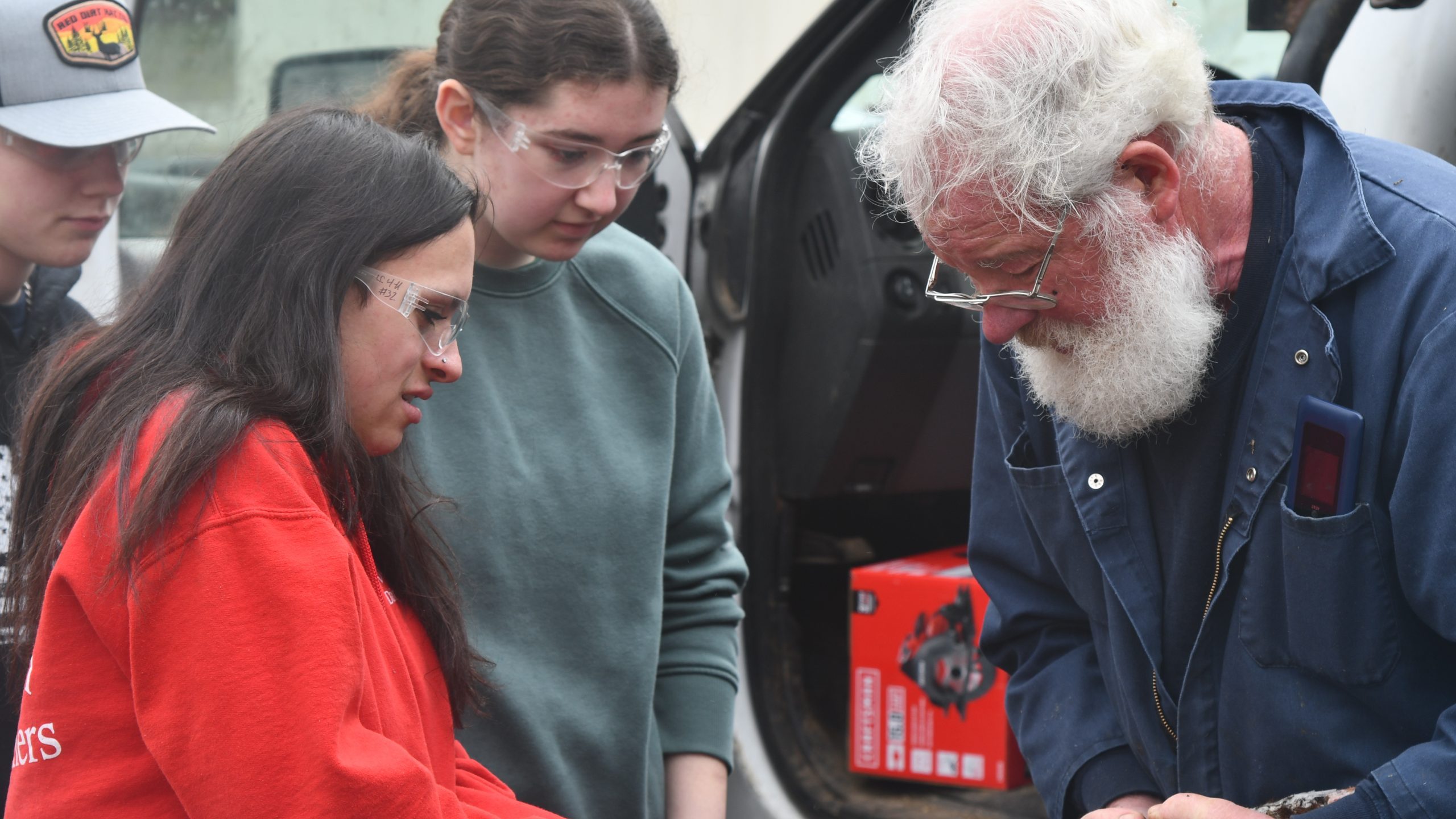 Girl using hoof tool on model hoof as man holds it 