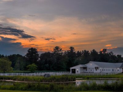 White barn near a pond with the sunsetting in the background