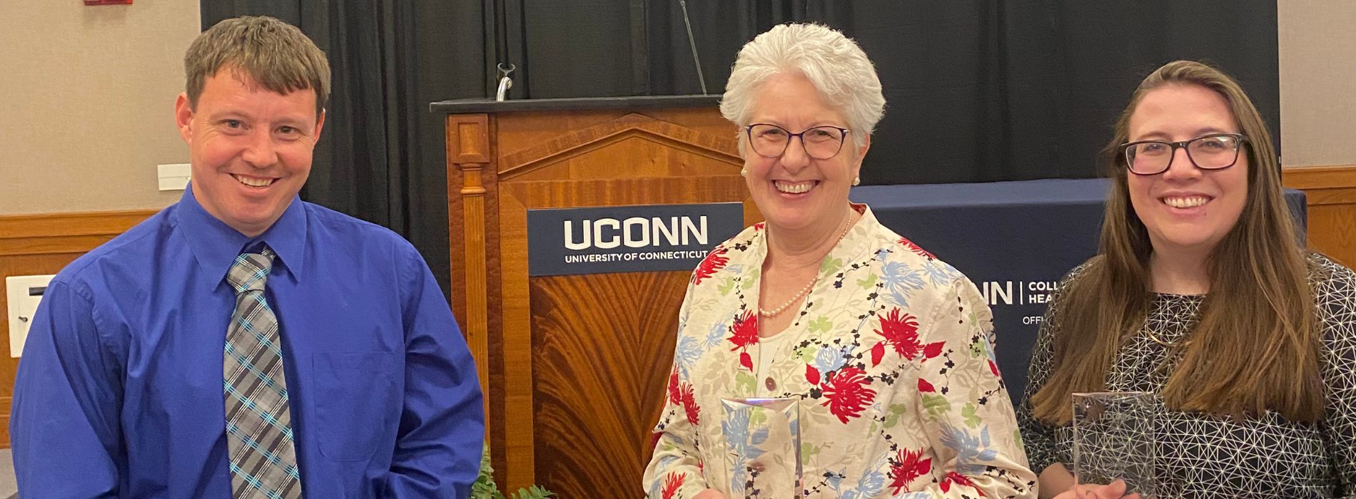 Three individuals holding awards with a UConn logo behind
